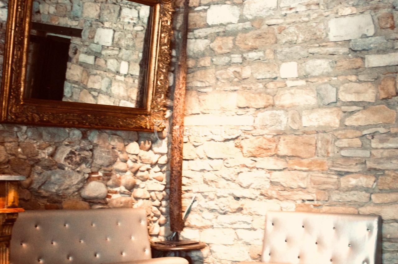 Deux canapés gris capitonnés devant un mur en pierres apparentes avec un grand miroir doré.