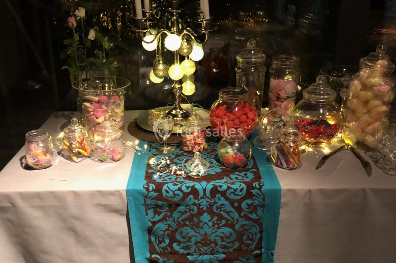 Table décorée avec un chemin de table turquoise, des bonbonnières remplies de sucreries et un chandelier allumé.