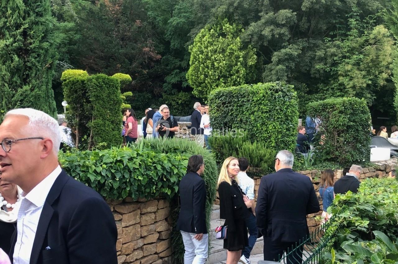 Personnes discutant dans un jardin aménagé avec des haies et des arbres en arrière-plan.