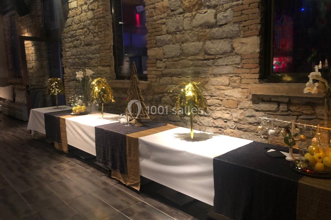 Table décorée avec nappes noires et blanches, ornée de plantes dorées, citrons et objets décoratifs, devant un mur en pierre.