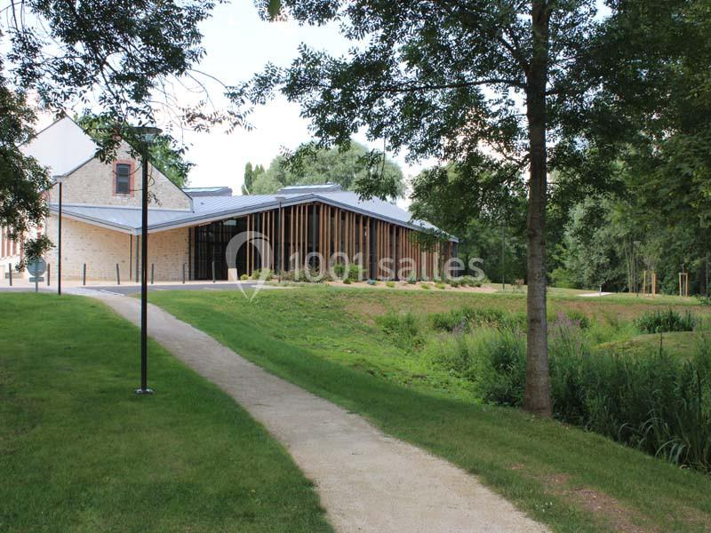 Bâtiment moderne avec façade en bois, entouré d'arbres et d'espaces verts, vu depuis un chemin en gravier.