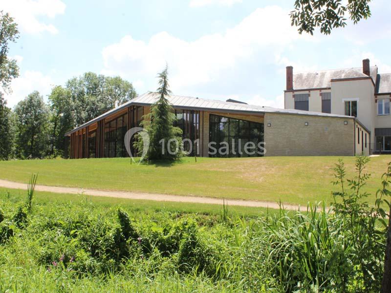 Bâtiment moderne avec façade vitrée et structure en bois, entouré de verdure et situé près d'un chemin.
