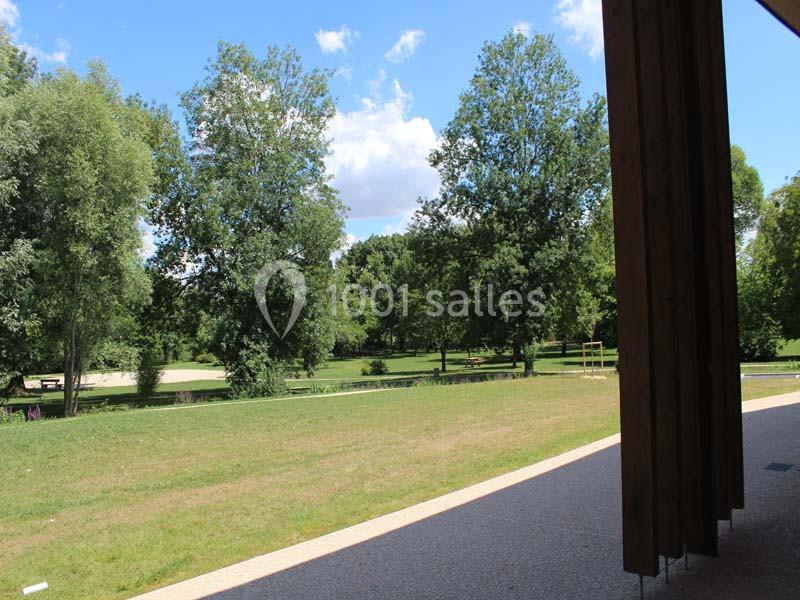 Vue sur un parc verdoyant avec des arbres et une pelouse, prise depuis un bâtiment en bois partiellement visible.