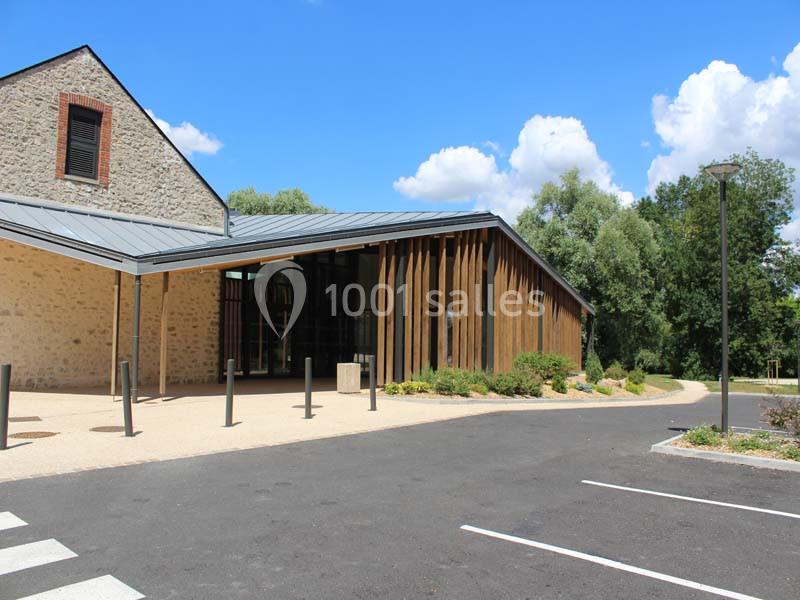 Bâtiment moderne avec façade en bois et toit métallique, entouré de végétation et d'un parking asphalté.