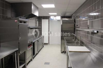 Cuisine professionnelle avec plans de travail en inox, équipements de cuisson, éviers et carrelage mural gris.