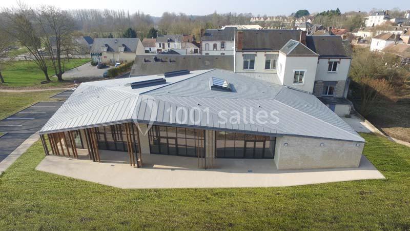 Vue aérienne d'un bâtiment moderne avec toit en métal, entouré de verdure et de maisons dans un environnement rural.