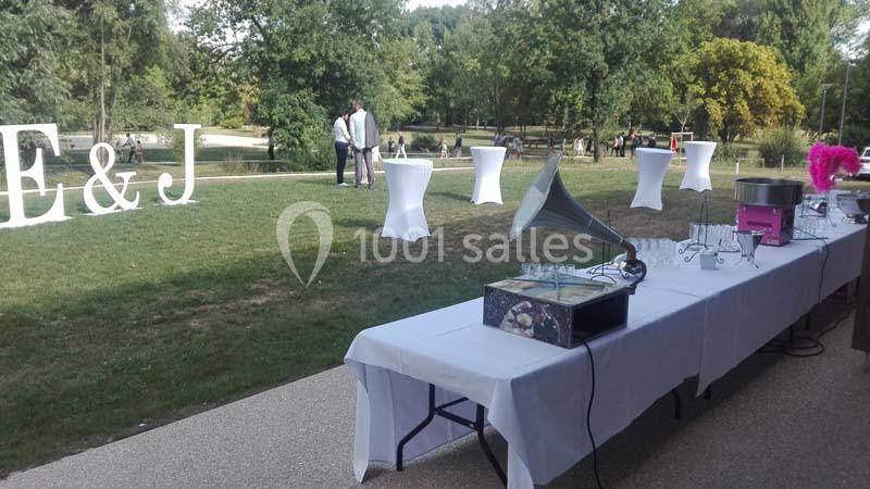 Tables dressées en extérieur avec un gramophone, des verres et une machine à barbe à papa, dans un parc verdoyant.