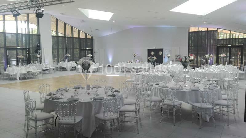 Salle de réception lumineuse avec tables rondes dressées, chaises transparentes et piste de danse au centre.