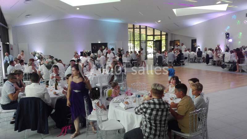 Salle de réception lumineuse avec des invités assis à des tables rondes, lors d'un événement festif.