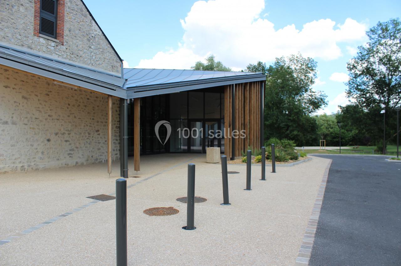 Entrée d'un bâtiment moderne avec façade en pierre, toit métallique et piliers en bois, entourée de végétation.