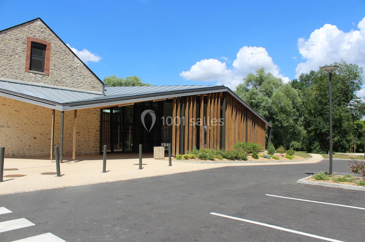 Bâtiment moderne avec façade en bois et toit métallique, entouré de végétation, sous un ciel bleu.
