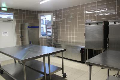 Cuisine professionnelle avec plans de travail en inox, équipements de cuisson, éviers et carrelage mural gris.