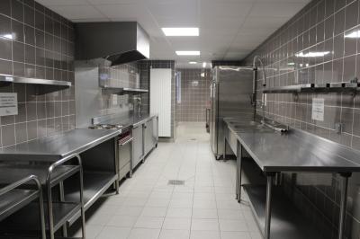 Cuisine professionnelle avec plans de travail en inox, équipements de cuisson, éviers et carrelage mural gris.