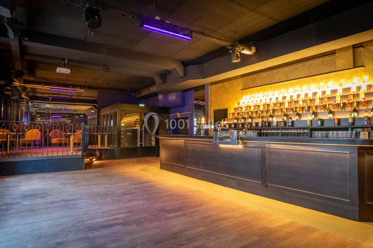 Bar moderne avec comptoir en bois sombre, étagères illuminées de bouteilles et ambiance tamisée.