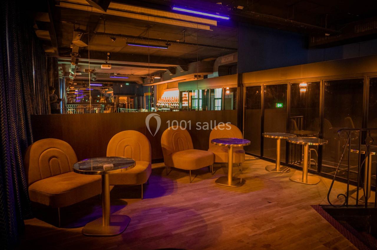 Espace lounge avec fauteuils orange, tables rondes et éclairage tamisé dans un décor intérieur moderne.