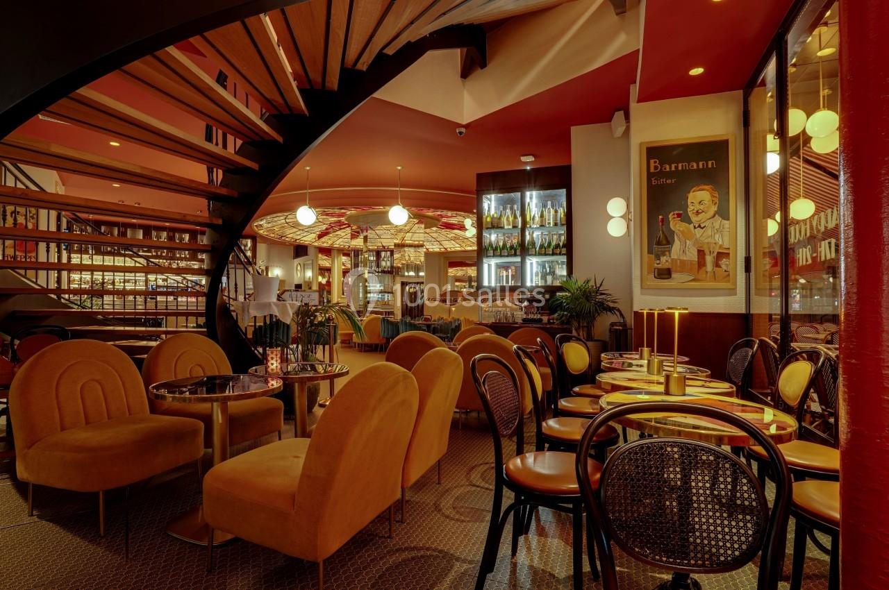 Intérieur d'un restaurant avec des tables, des chaises élégantes, un escalier en colimaçon et une ambiance chaleureuse.