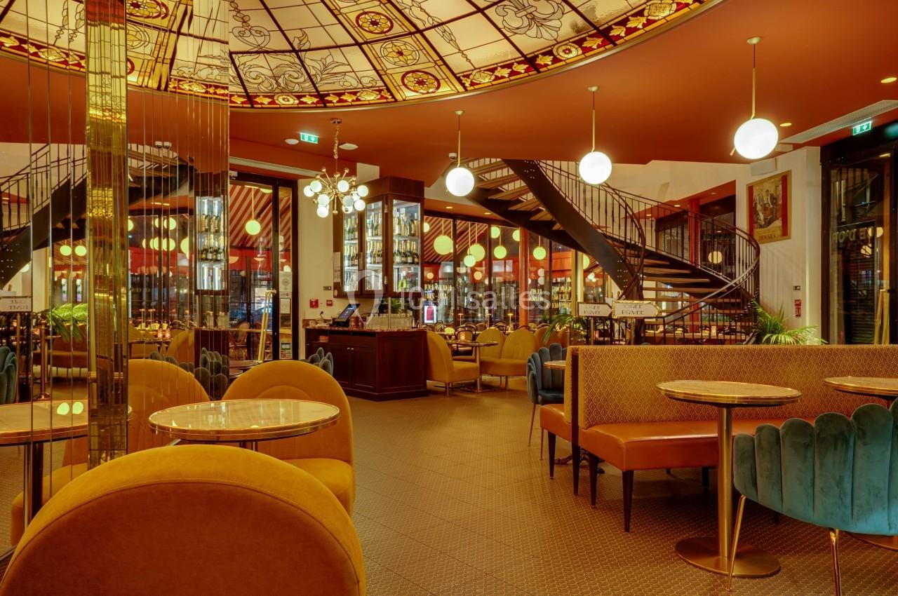 Intérieur d'un café élégant avec des banquettes colorées, des tables rondes et un escalier menant à l'étage.