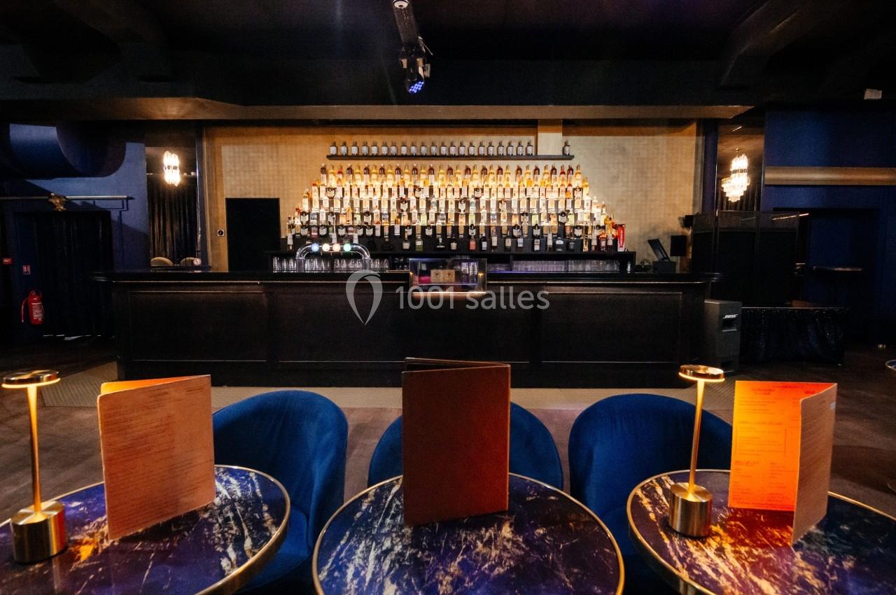 Bar élégant avec un large comptoir en bois, des étagères remplies de bouteilles et des tables avec lampes et menus au…