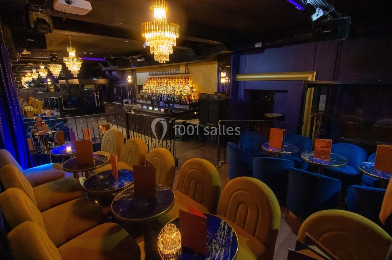 Salle de bar élégante avec tables rondes, fauteuils colorés et lustres suspendus, éclairage tamisé.
