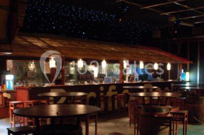 Salle de restaurant en bois avec tables dressées, chaises alignées et lumière naturelle entrant par de grandes fenêtres.