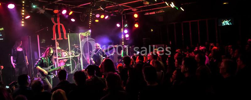 Groupe de musiciens jouant sur scène devant un public sous des éclairages colorés dans une ambiance de concert.