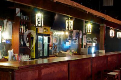 Salle de restaurant en bois avec tables dressées, chaises alignées et lumière naturelle entrant par de grandes fenêtres.