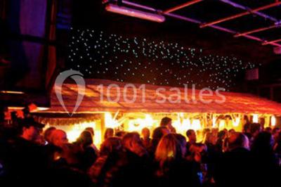 Salle de restaurant en bois avec tables dressées, chaises alignées et lumière naturelle entrant par de grandes fenêtres.