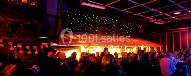 Salle sombre avec des lumières tamisées, un toit de chaume éclairé et des personnes rassemblées en groupe.