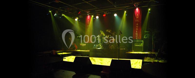 Scène de concert éclairée avec une batterie, des guitares et des amplificateurs sous des projecteurs colorés.