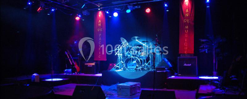Scène de concert éclairée en bleu avec une batterie au centre, des amplificateurs et des guitares en arrière-plan.