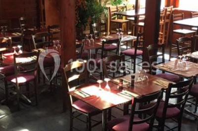 Salle de restaurant en bois avec tables dressées, chaises alignées et lumière naturelle entrant par de grandes fenêtres.