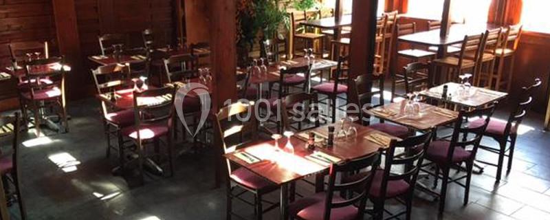 Salle de restaurant avec des tables en bois dressées, éclairée par la lumière naturelle provenant des fenêtres.