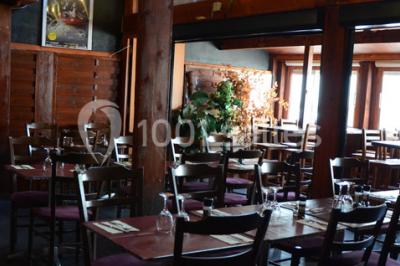 Salle de restaurant en bois avec tables dressées, chaises alignées et lumière naturelle entrant par de grandes fenêtres.