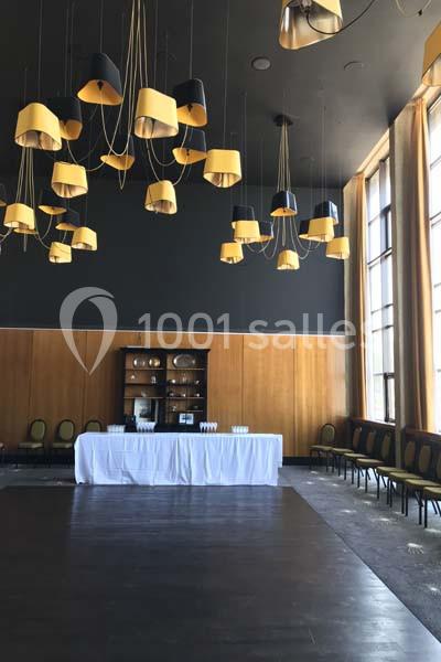 Salle avec un plafond sombre, des suspensions jaunes et noires, des murs en bois, et une table blanche dressée.
