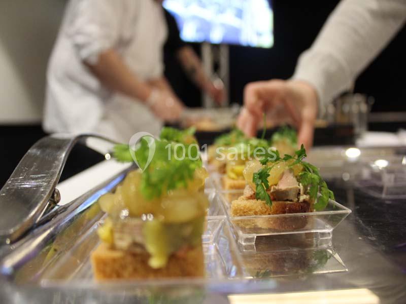 Des amuse-bouches garnis de viande, condiments et herbes fraîches sont présentés dans des verrines sur un plateau.