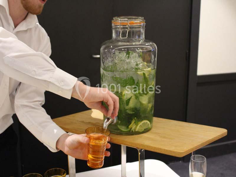 Un serveur remplit un verre avec une boisson fraîche à base de citron, menthe et glaçons, depuis un grand distributeur en…