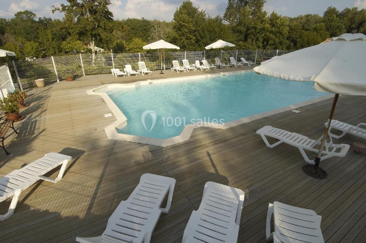 Piscine extérieure entourée de chaises longues blanches, parasols et végétation en arrière-plan.