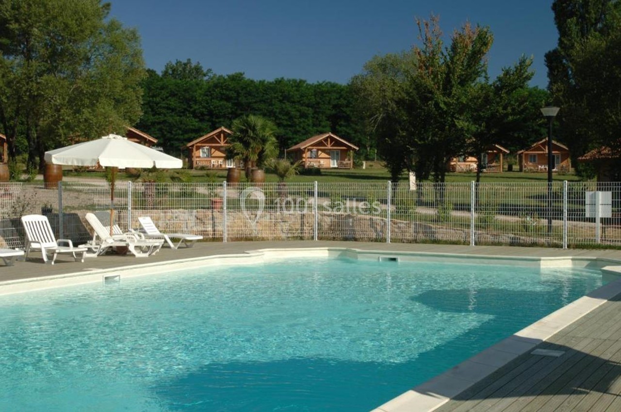 Piscine extérieure entourée de chaises longues, parasols et vue sur des chalets en bois dans un cadre verdoyant.