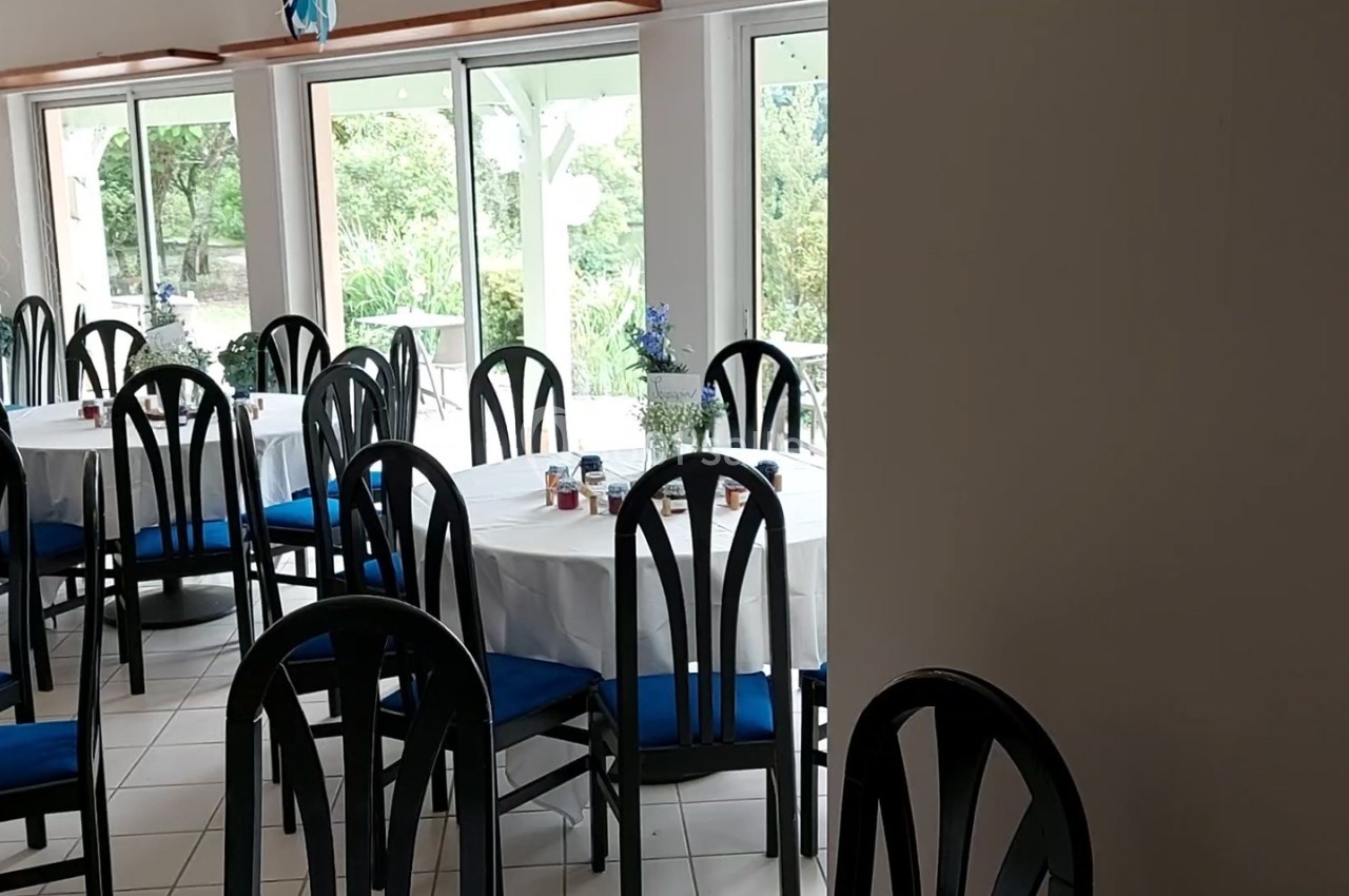 Salle de réception lumineuse avec des tables rondes dressées, chaises noires et fenêtres donnant sur un jardin verdoyant.