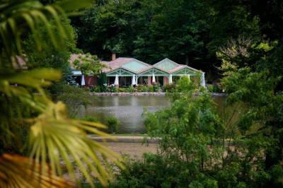 Salle de réception décorée avec des tables rondes, nappes blanches et chaises habillées, donnant sur un jardin extérieur.