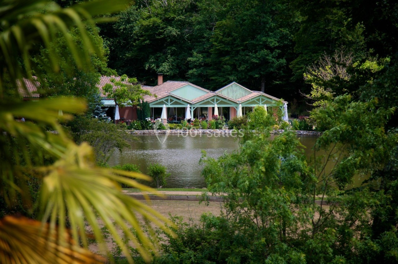 Maison avec toit en tuiles et véranda, située au bord d'un étang entouré de végétation dense.