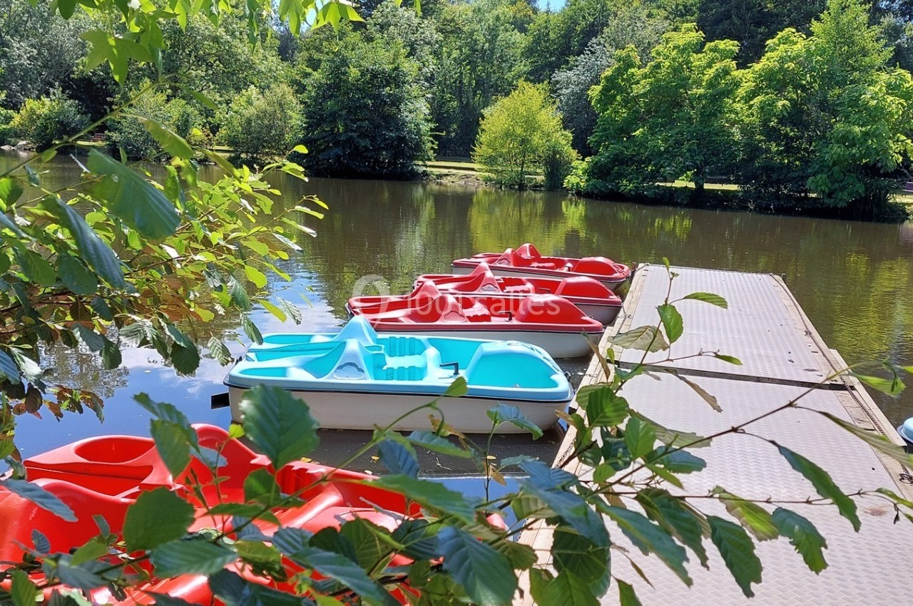 Pédalos rouges et bleus amarrés à un ponton en bois sur un étang entouré de végétation verdoyante.