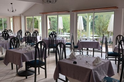 Salle de réception décorée avec des tables rondes, nappes blanches et chaises habillées, donnant sur un jardin extérieur.