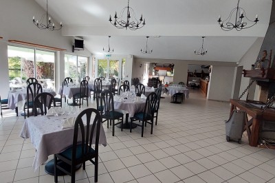 Salle de réception décorée avec des tables rondes, nappes blanches et chaises habillées, donnant sur un jardin extérieur.