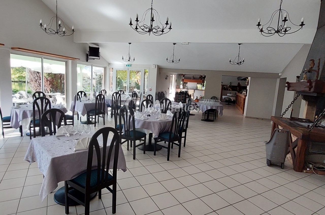 Salle de restaurant lumineuse avec tables dressées, chaises noires et cheminée décorative dans un cadre spacieux.