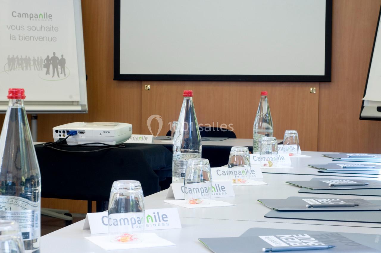 Salle de réunion équipée avec projecteur, tableau de conférence, bouteilles d'eau et dossiers disposés sur une table.
