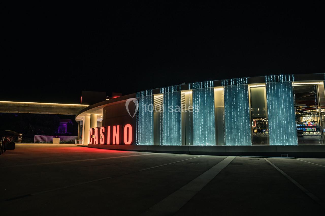Façade d'un casino illuminé la nuit avec des lumières bleues et rouges, vue depuis un parking vide.
