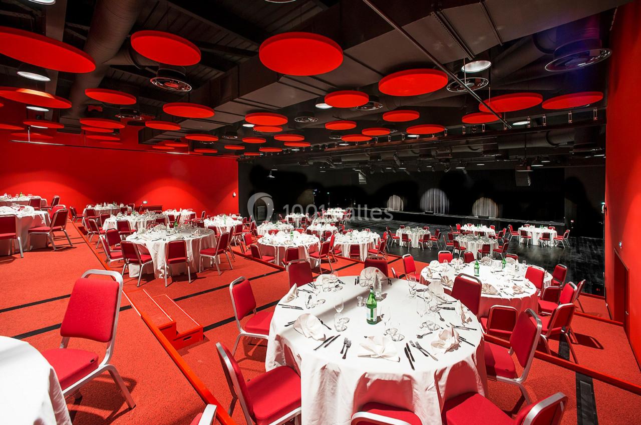 Salle de réception avec tables rondes dressées, chaises rouges et plafond décoré de panneaux acoustiques rouges.