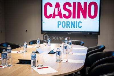 Bâtiment moderne en bord de rivière, entouré de verdure, avec un pont piétonnier au premier plan.