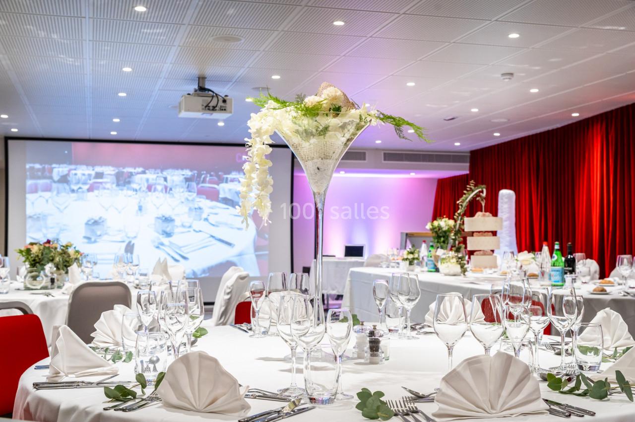Salle de réception décorée avec des tables dressées, un grand centre de table floral et un écran en arrière-plan.